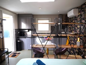 A compact kitchen with a central island, a dining area with a chair, and a bed with a pillow.