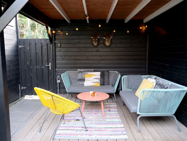 An outdoor seating area with a sofa, chairs, and a table, featuring a wooden ceiling and a view through a wooden door.