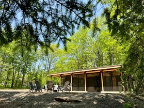 Een moderne cabin met een overdekt terras, buitenmeubels en uitzicht op het omliggende bos.