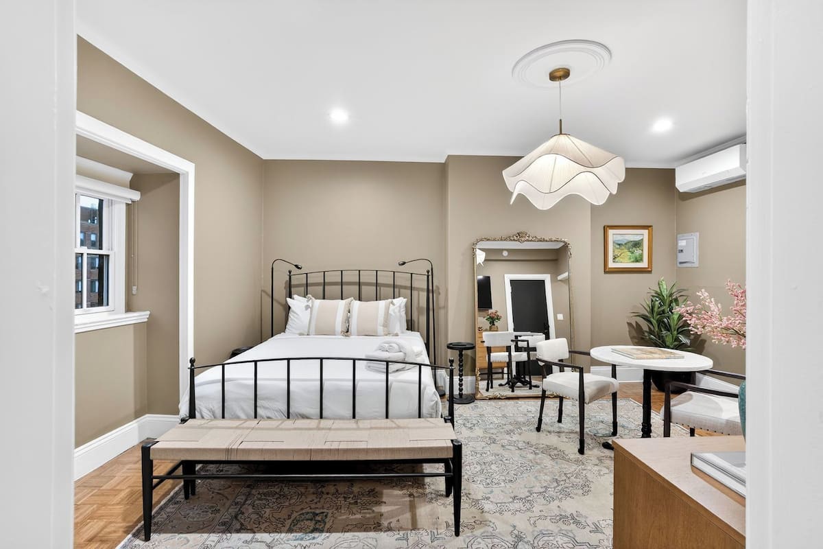 A bedroom with a bed, bedside table, chair, and a large mirror.