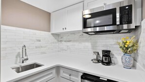 Una cocina moderna con armarios blancos, un microondas de acero inoxidable, una cafetera y un florero con flores.