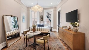 Una habitación con una cama, una mesa redonda con sillas, un aparador, un espejo y un televisor en la pared.
