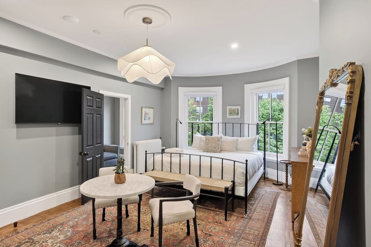 A bedroom with a bed, bedside table, chair, and a large window.