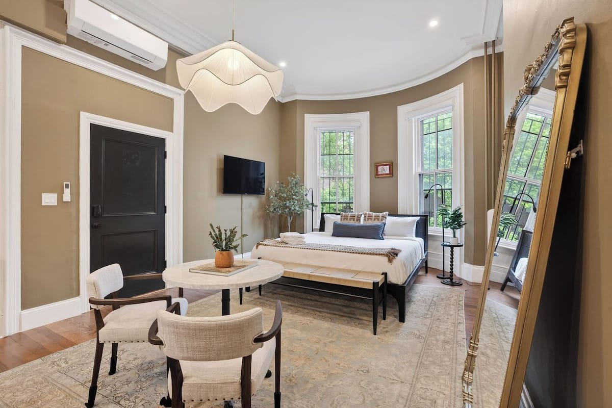 A bedroom with a bed, a round table with chairs, a TV, and a large mirror.