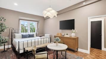 A bedroom with a bed, bedside table, chair, round table, dresser, TV, and a door.