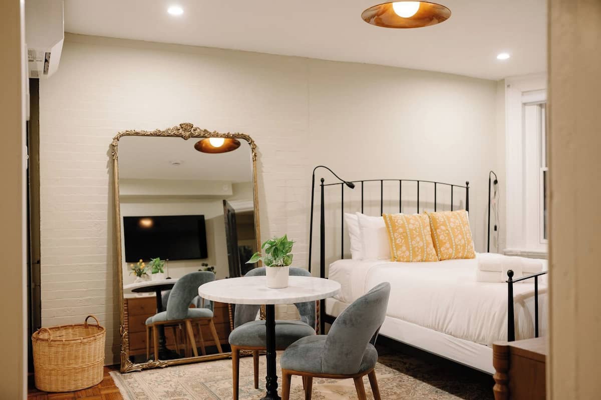 A bedroom with a bed, bedside table, mirror, round table, chairs, and a television.