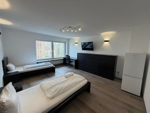 Een moderne slaapkamer met een bed, bureau, televisie en een koelkast.