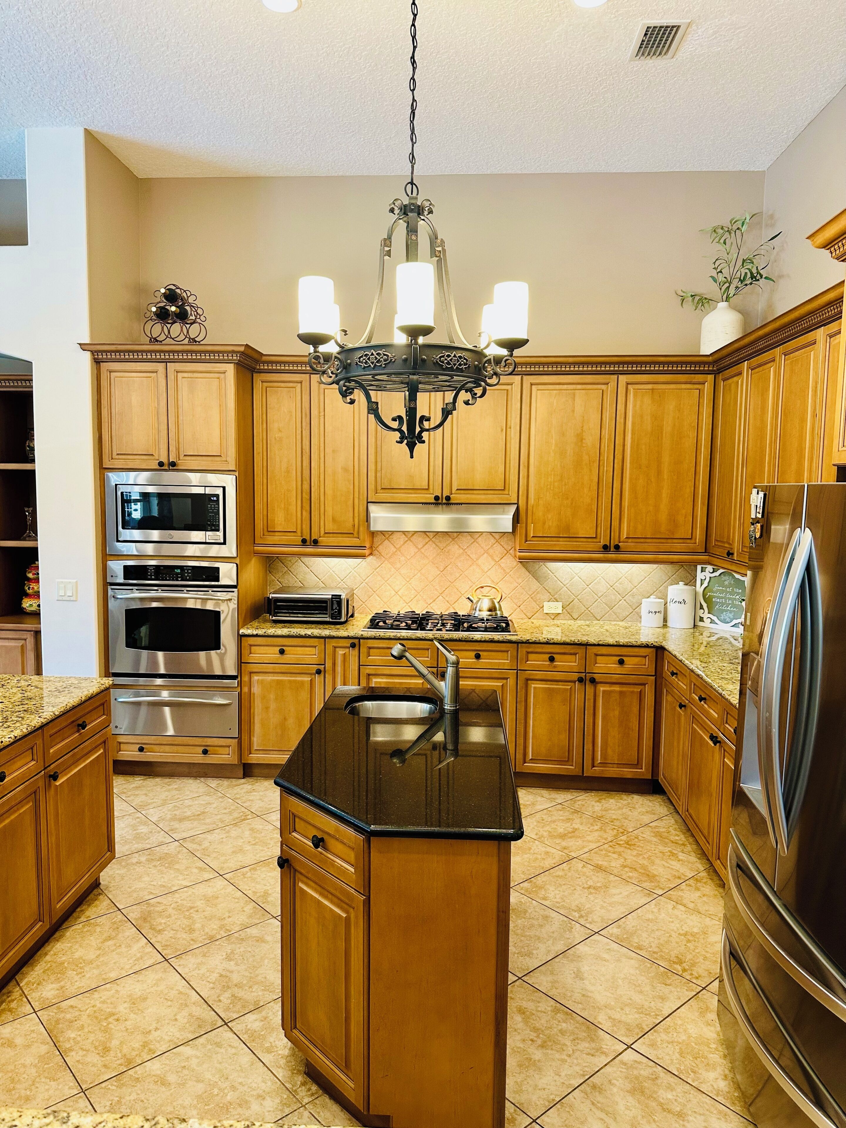 A kitchen with wooden cabinets, stainless steel appliances, a black granite countertop, and a chandelier.