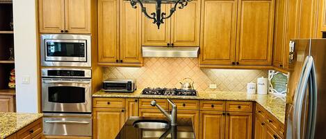A kitchen with wooden cabinets, stainless steel appliances, a black granite countertop, and a chandelier.