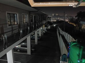 A multi-level parking structure with cars parked on different levels, a balcony with a railing, and a view of a cityscape at night. - Crompton Studio Apartment 786 (Durban)