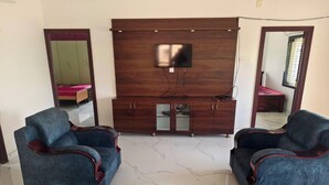 Una sala de estar con dos sofás azules, un mueble de madera para el entretenimiento con un televisor y un espejo en la pared.