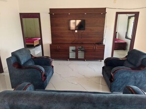 Un salon avec deux canapés bleus, un meuble de rangement en bois sur lequel est posée une télévision, et un miroir accroché au mur.