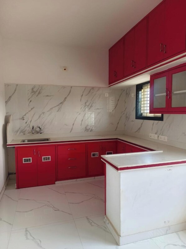 Una cocina con gabinetes rojos, encimera blanca y salpicadero de mármol.