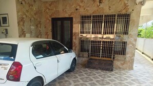 Un coche blanco estacionado frente a un edificio con suelo de baldosas y entrada protegida con barrotes.