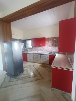 Una cocina con armarios rojos, un refrigerador de acero inoxidable y un salpicadero de azulejos.