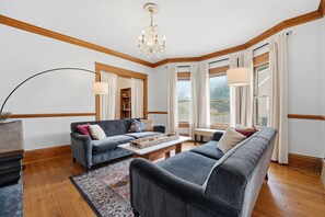 Ein Wohnzimmer mit einer Chandelier, zwei Sofas, einem Couchtisch und großen Fenstern mit Vorhängen.