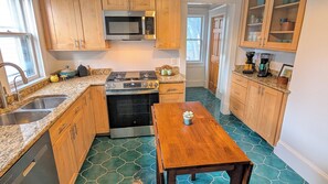 A kitchen with wooden cabinets, a stove, a microwave, a sink, and a dining table with a potted plant. - World Cup Stay! Historic KC Charmer Near KU Med & 39th Street (Kansas City)