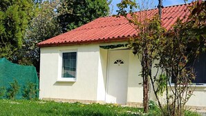 A small white building with a red roof, surrounded by green grass and dandelions.
