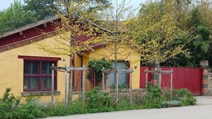 A yellow building with a red door and window frames, surrounded by greenery. - Les Bambous Vacation Rental, for 2 people, downtown Billom (one pet allowed) (Billom)