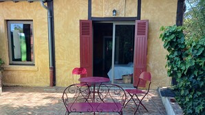 A patio with a table and chairs, a sliding glass door, and a window with a curtain. - Les Bambous Vacation Rental, for 2 people, downtown Billom (one pet allowed) (Billom)