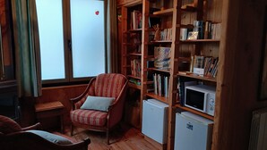 A cozy room with a wooden bookshelf, a striped armchair, a small table, and a white refrigerator. - Les Bambous Vacation Rental, for 2 people, downtown Billom (one pet allowed) (Billom)