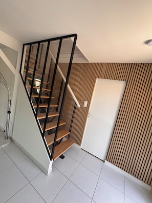 Eine Treppe mit Holzdielen und schwarzen Geländern, eine weiße Tür und eine Wand mit vertikalen Holzleisten.