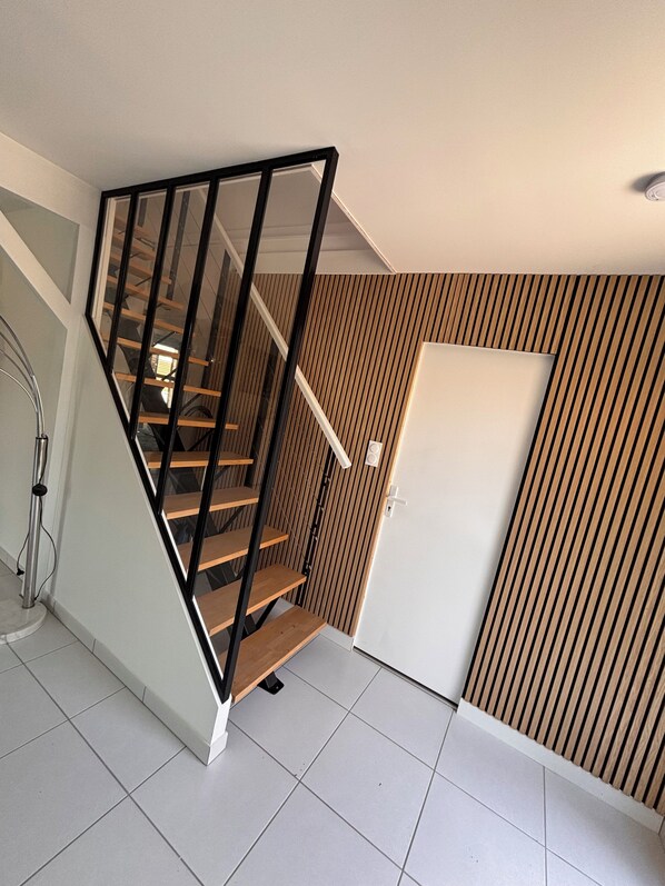 Eine Treppe mit Holzdielen und schwarzen Geländern, eine weiße Tür und eine Wand mit vertikalen Holzleisten.