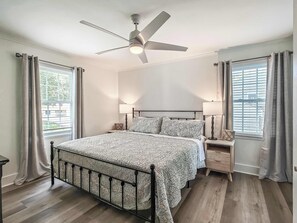 Une chambre à coucher avec un lit, un ventilateur de plafond, des lampes de chevet, une table de chevet et des rideaux.