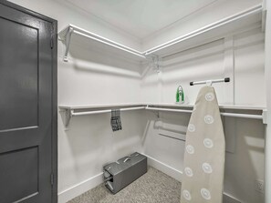 A compact, well-lit storage closet with shelves, a hanging rack, and a compact iron.