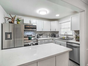 Une cuisine moderne avec des meubles blancs, des appareils en acier inoxydable et un îlot central.