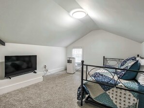 A bedroom with a TV, a bed with patterned bedding, a radiator, and a ceiling light.