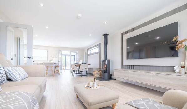 A modern living room with a sofa, ottoman, and a TV mounted on the wall. - Luxury House in Templepatrick I Big Garden I Near Airport & Belfast (Templepatrick)