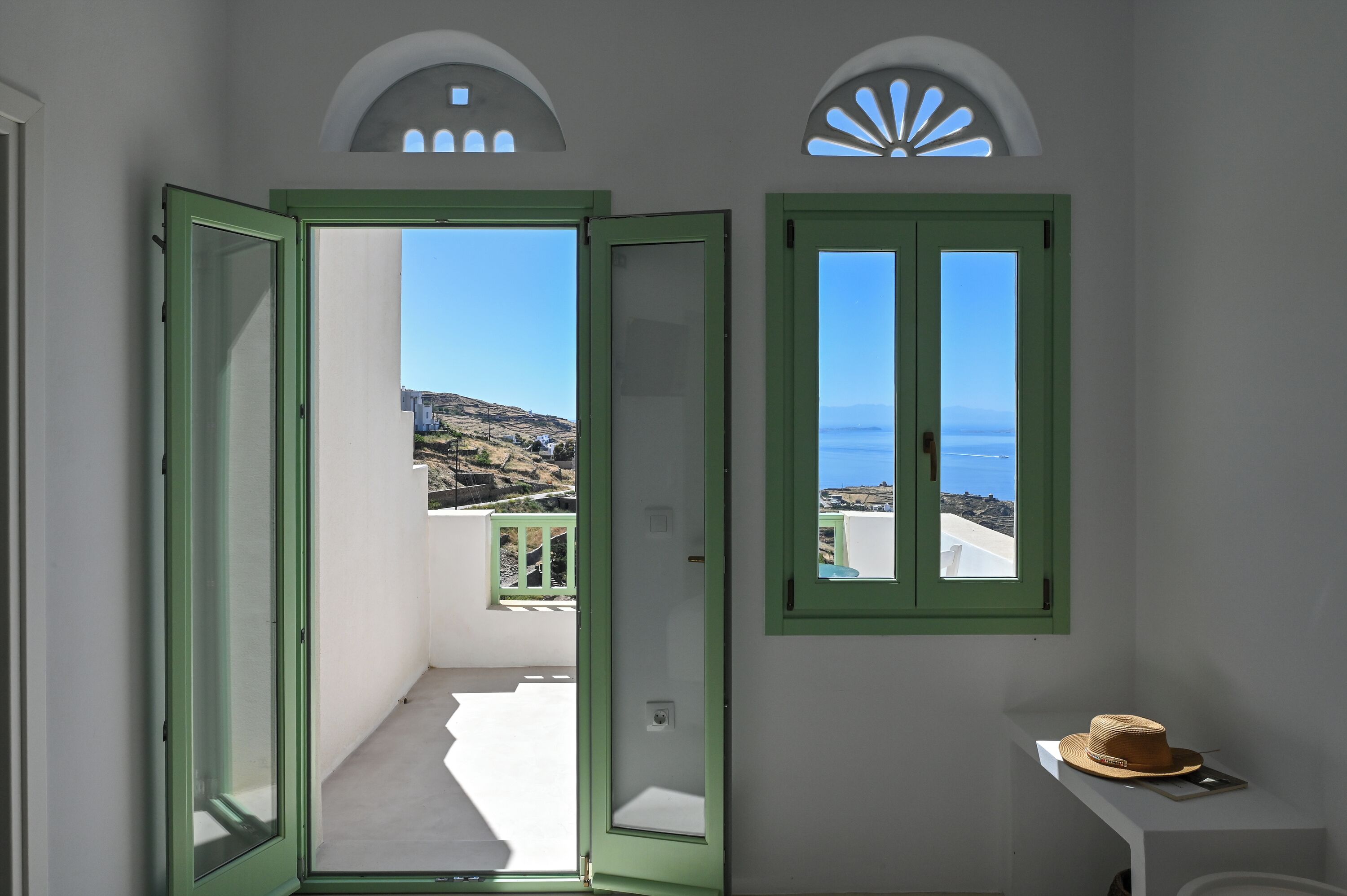 Ein Zimmer mit Balkon, ein Hut auf einem kleinen Tisch und Meerblick.