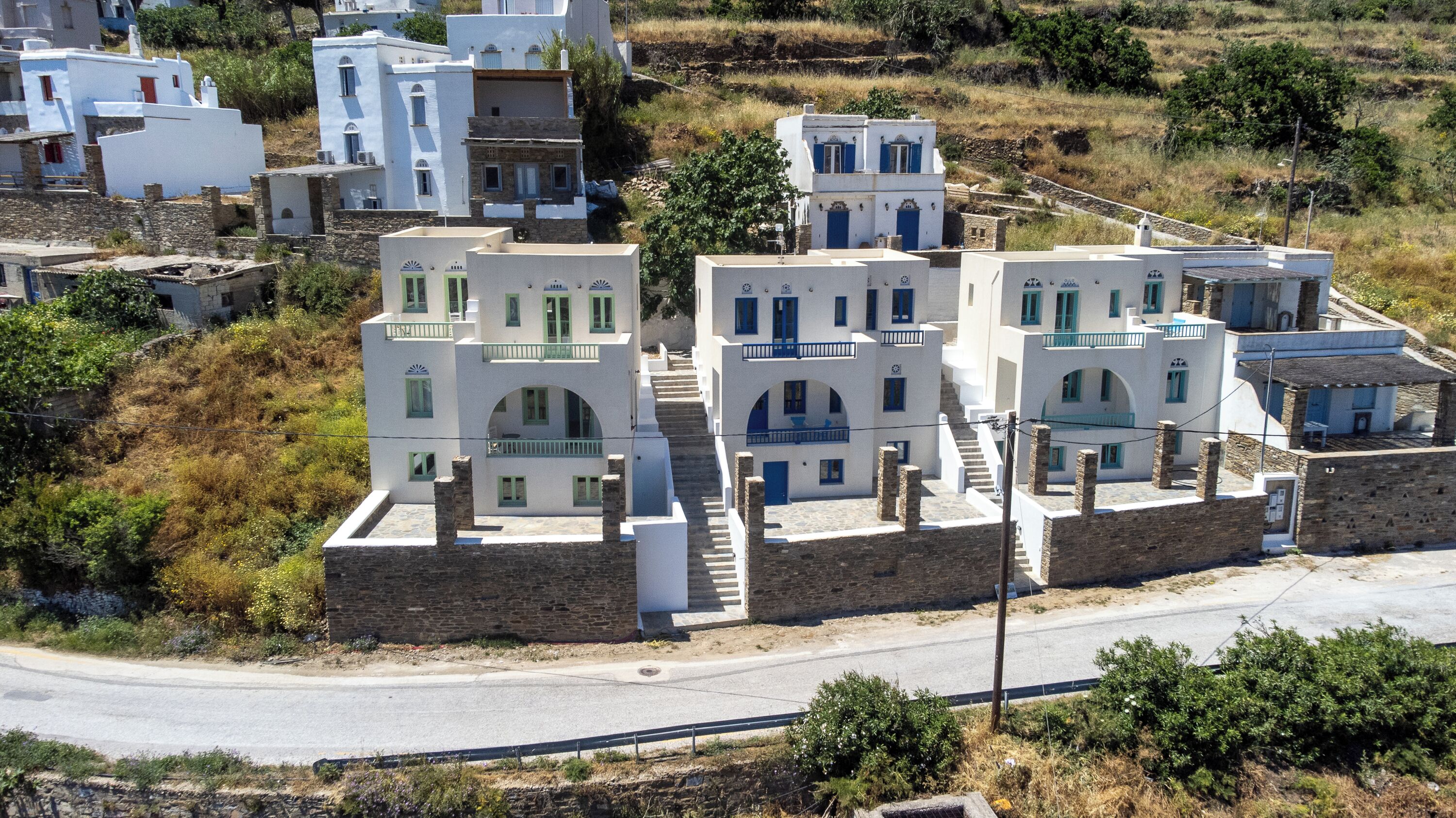 A cluster of white buildings with blue accents, stone walls, and a paved road in the foreground.