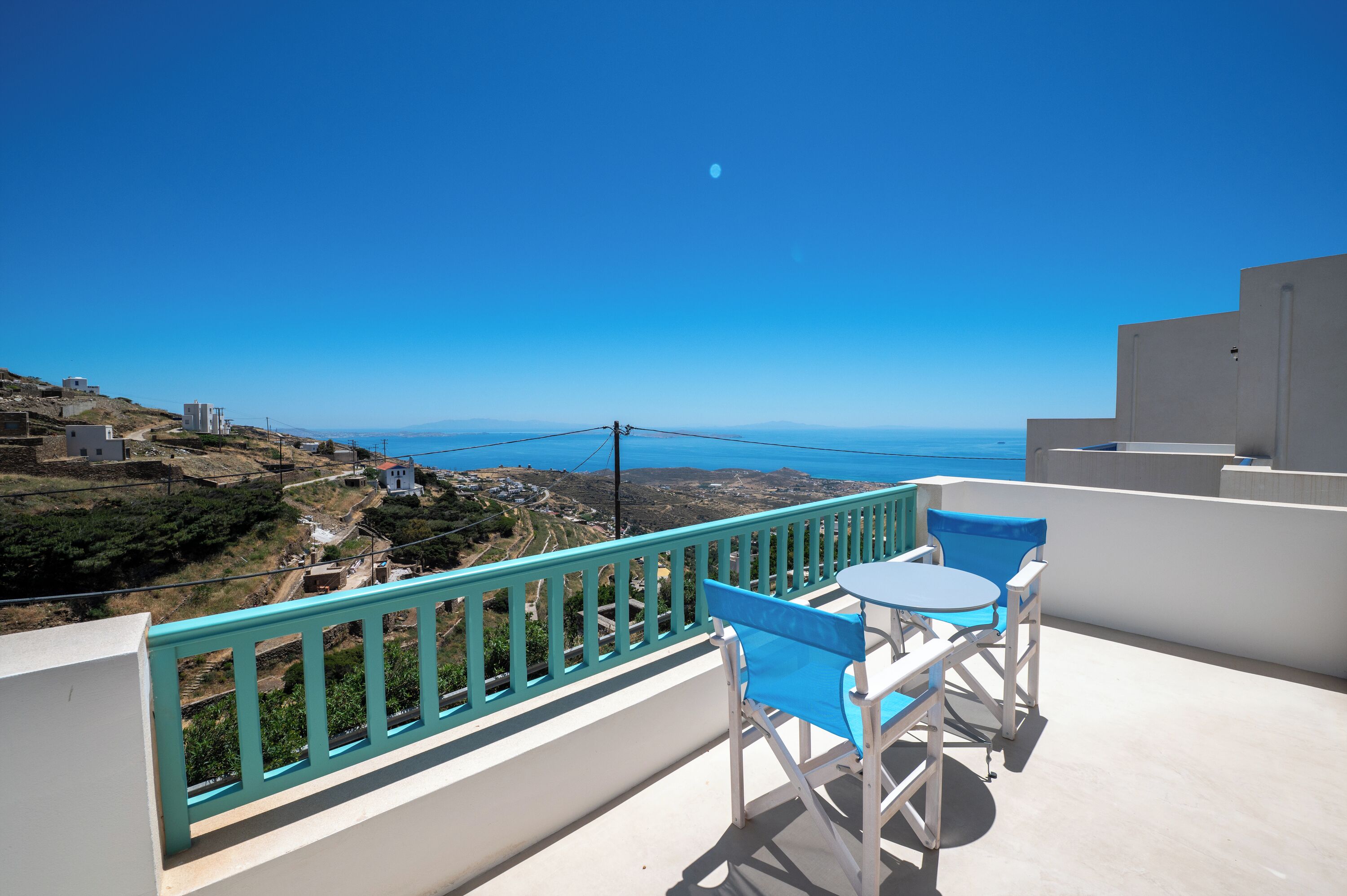 A balcony with a view of the sea, a table with chairs, and a turquoise railing.