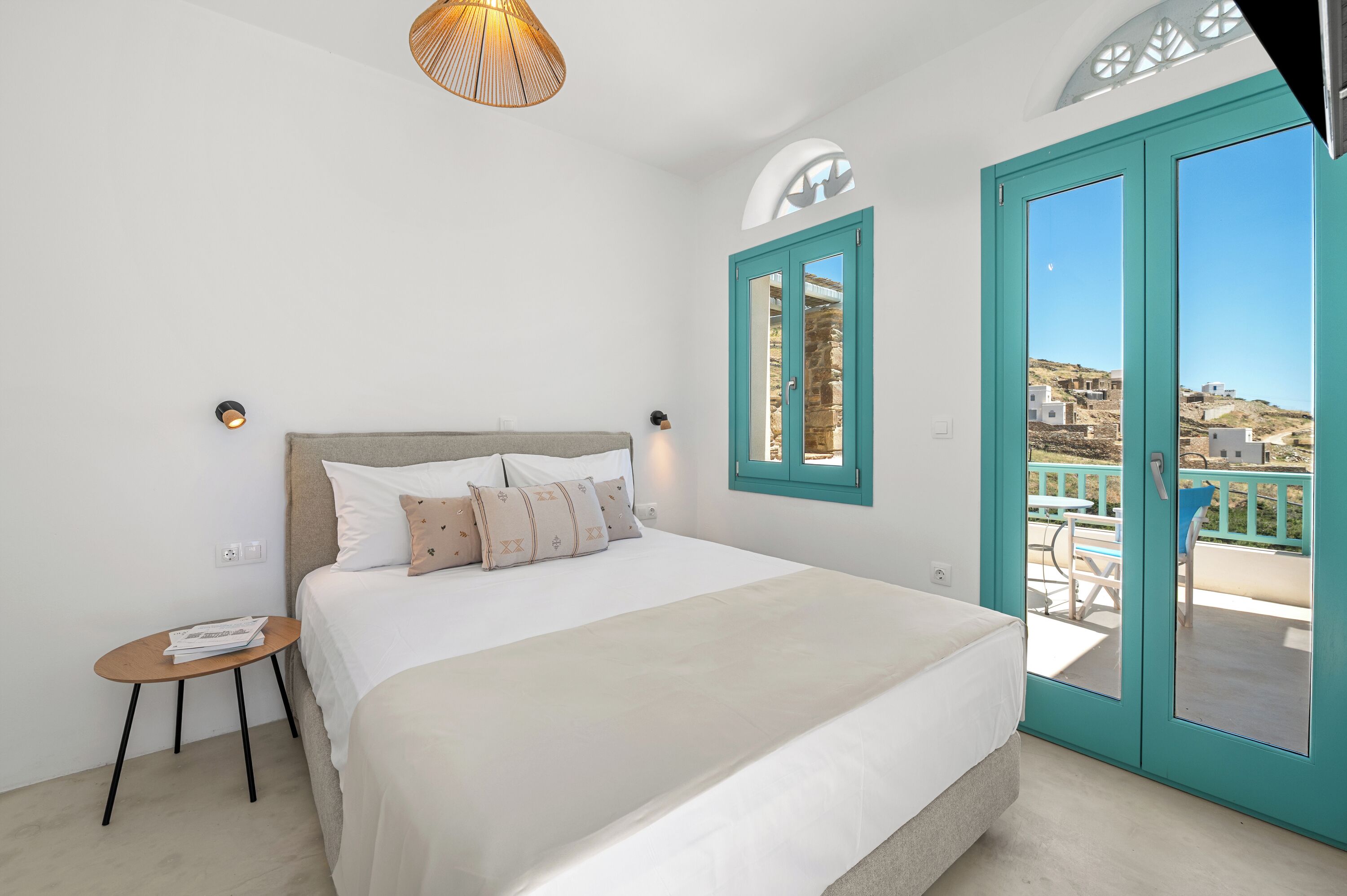 Une chambre avec un lit, une petite table, une fenêtre donnant sur un paysage agréable et une porte qui mène à un espace extérieur.