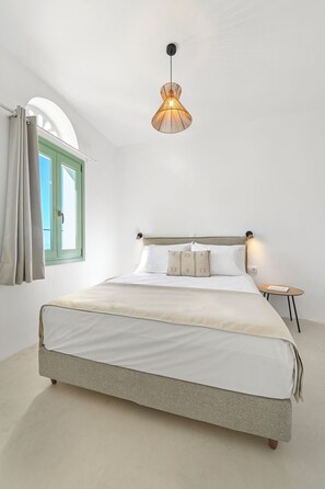 A bedroom with a bed, a window with curtains, a hanging light fixture, and a bedside table. - Arnados Tinos Rooms by Tinosstay (Tinos)
