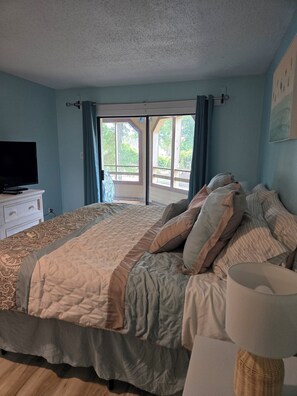 A bedroom with a bed, a television, a lamp, and a view of the outdoors. - Ocean Ahh, a beautiful 2 BR/2 BA condo less than .4 miles to the beach (Myrtle Beach)