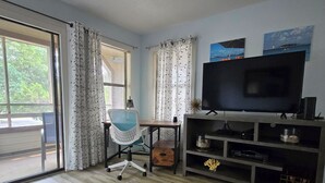 Ein Wohnzimmer mit einer Couch, einem Fernseher, einem Schreibtisch und einem Sessel.