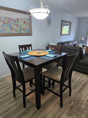 A dining area with a wooden table, dark chairs, a hanging light fixture, a colorful painting on the wall, and a star-shaped decoration. - Ocean Ahh, a beautiful 2 BR/2 BA condo less than .4 miles to the beach (Myrtle Beach)