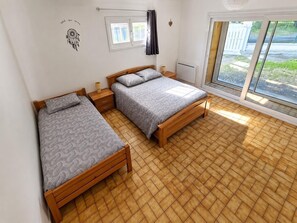 Ein Schlafzimmer mit zwei Einzelbetten, einem Fenster mit Vorhängen, einem Heizkörper und Blick ins Freie.