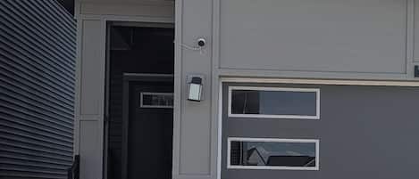 Une maison moderne à deux étages, dotée d’un garage, d’une porte d’entrée et d’un petit porche.