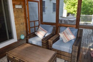 A covered porch with wicker furniture and a table, a wooden door, and a window with blinds. - Quiet North Conway home: Hot tub, arcade, outlets! (Conway)