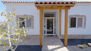 Ein Haus mit Ziegeldach, einem gepflasterten Eingangsbereich und zwei Fenstern mit Steinrahmen.