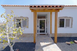 Ein Haus mit Ziegeldach, einem gepflasterten Eingangsbereich und zwei Fenstern mit Steinrahmen.