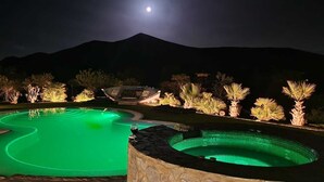 Ein Schwimmbeckenbereich bei Nacht mit Bergblick und einem sichtbaren Mond.