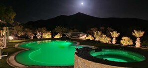 Ein Schwimmbeckenbereich bei Nacht mit Bergblick und einem sichtbaren Mond.