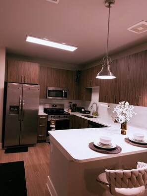 Une cuisine moderne avec des meubles en bois, des appareils électroménagers en acier inoxydable, un îlot central agrémenté d’un vase de fleurs et un luminaire suspendu.