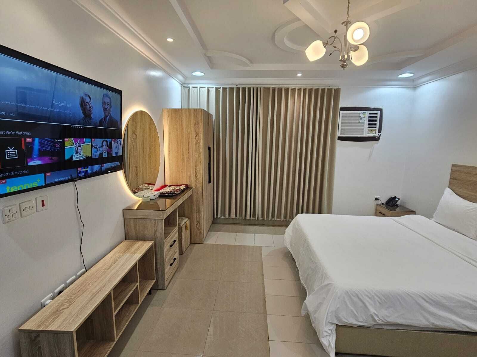 Une chambre d’hôtel moderne équipée d’un grand téléviseur à écran plat, d’un bureau en bois, d’un lit et d’un luminaire fixé au plafond.