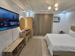 Ein modernes Hotelzimmer mit einem großen Flachbildfernseher, einem Holztisch, einem Bett und einer Deckenleuchte.